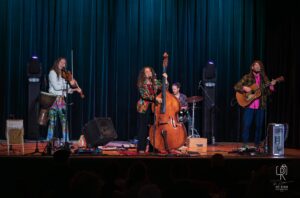 Live Quartet Performance on Stage Musicians perform with violin, upright bass, drums, and guitar on a dimly lit stage.