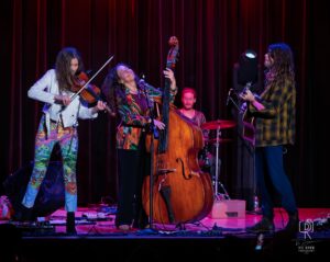 Colorful Stage Performance by Musical Quartet Musicians perform energetically on stage with vibrant lighting and colorful backdrop.