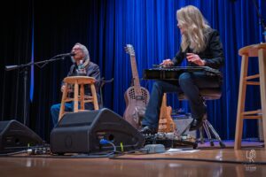Acoustic and Lap Steel Guitar Performance Stage performance with two musicians playing guitar and lap steel, surrounded by blue curtains.