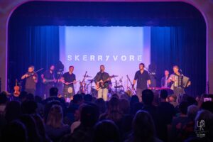 Skerryvore Live Performance Band performs on stage with guitar, violin, accordion; backdrop reads "Skerryvore."