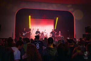 Concert Performance with Vibrant Lighting Band performing live on stage with crowd and red-yellow lighting; instruments include violin, keyboard.